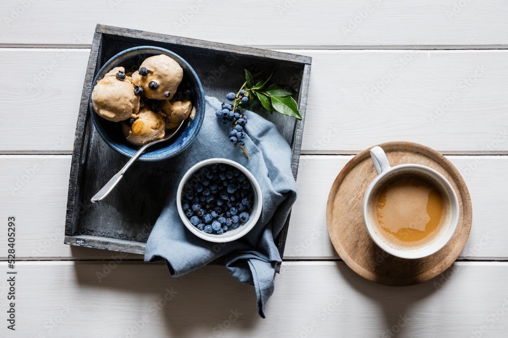 Cup of coffee and tray with fresh blueberries and homemade peanut ice cream
