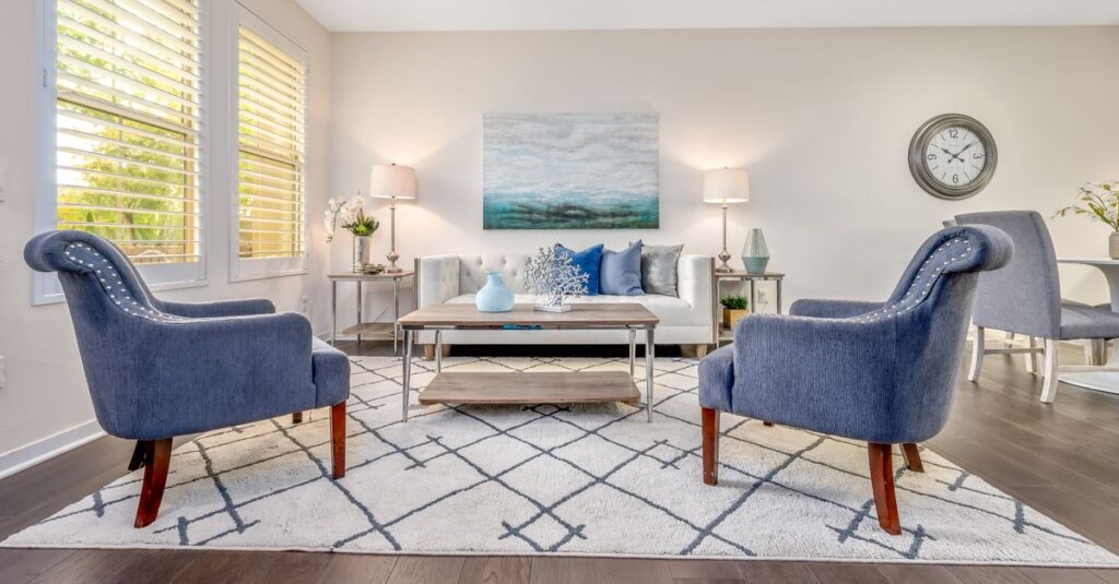 A bright living room with a pale sofa, blue armchairs and a large patterned area rug covering the floor.