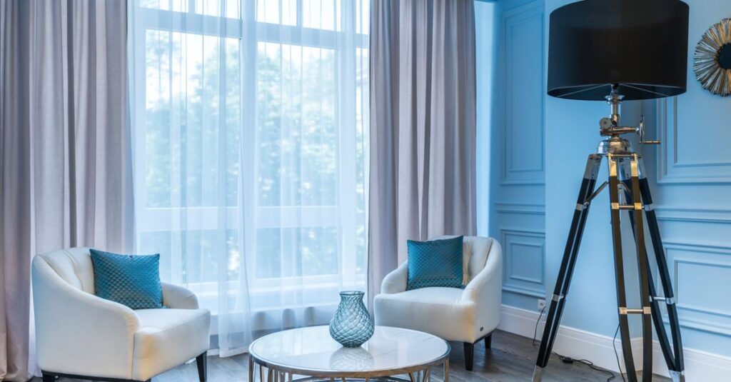 A bright living room corner with white armchairs and a tall black tripod floor lamp.