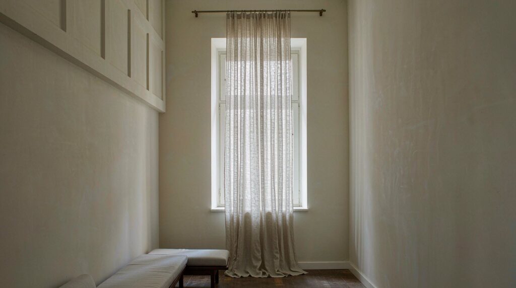 Tall window in a room with a high ceiling, sheer linen curtains hung from a rod well above the window frame and dropping to the floor