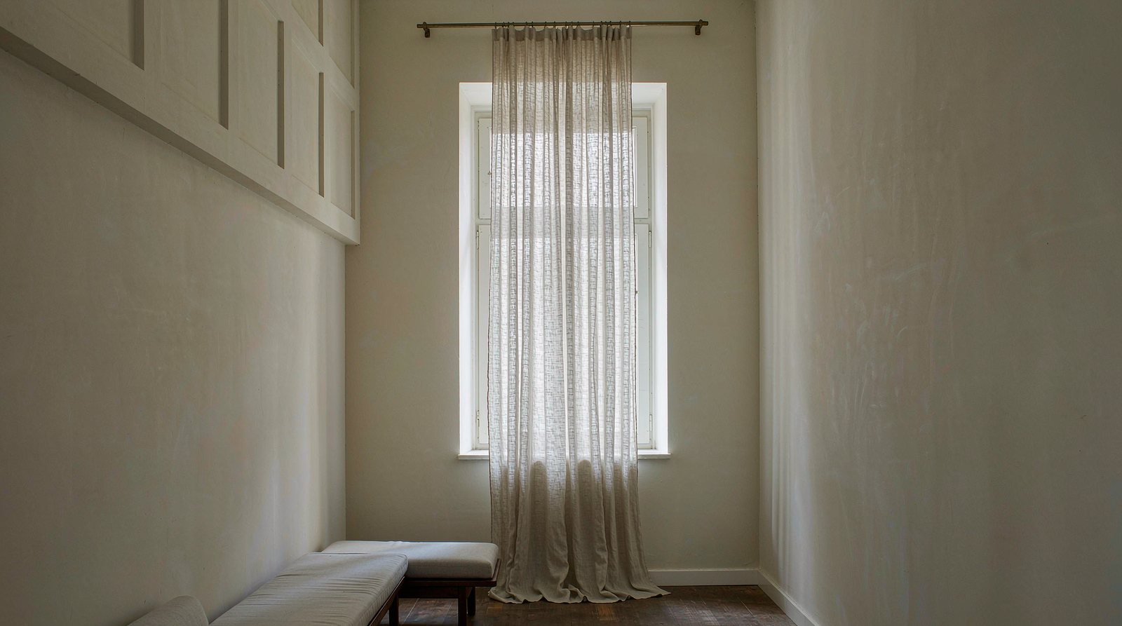 Tall window in a room with a high ceiling, sheer linen curtains hung from a rod well above the window frame and dropping to the floor