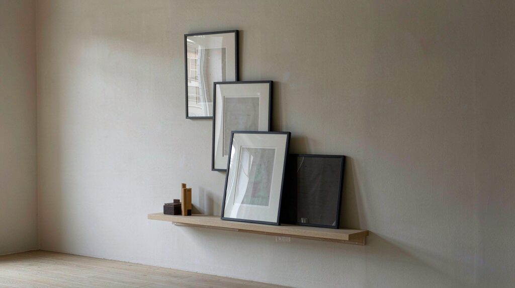 Plain cream wall with a wooden picture ledge holding small framed prints, fixed with adhesive and no holes or nails