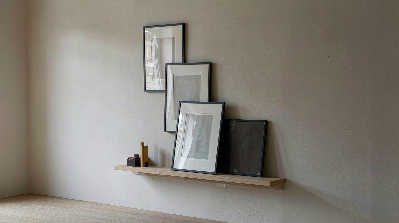 Plain cream wall with a wooden picture ledge holding small framed prints, fixed with adhesive and no holes or nails