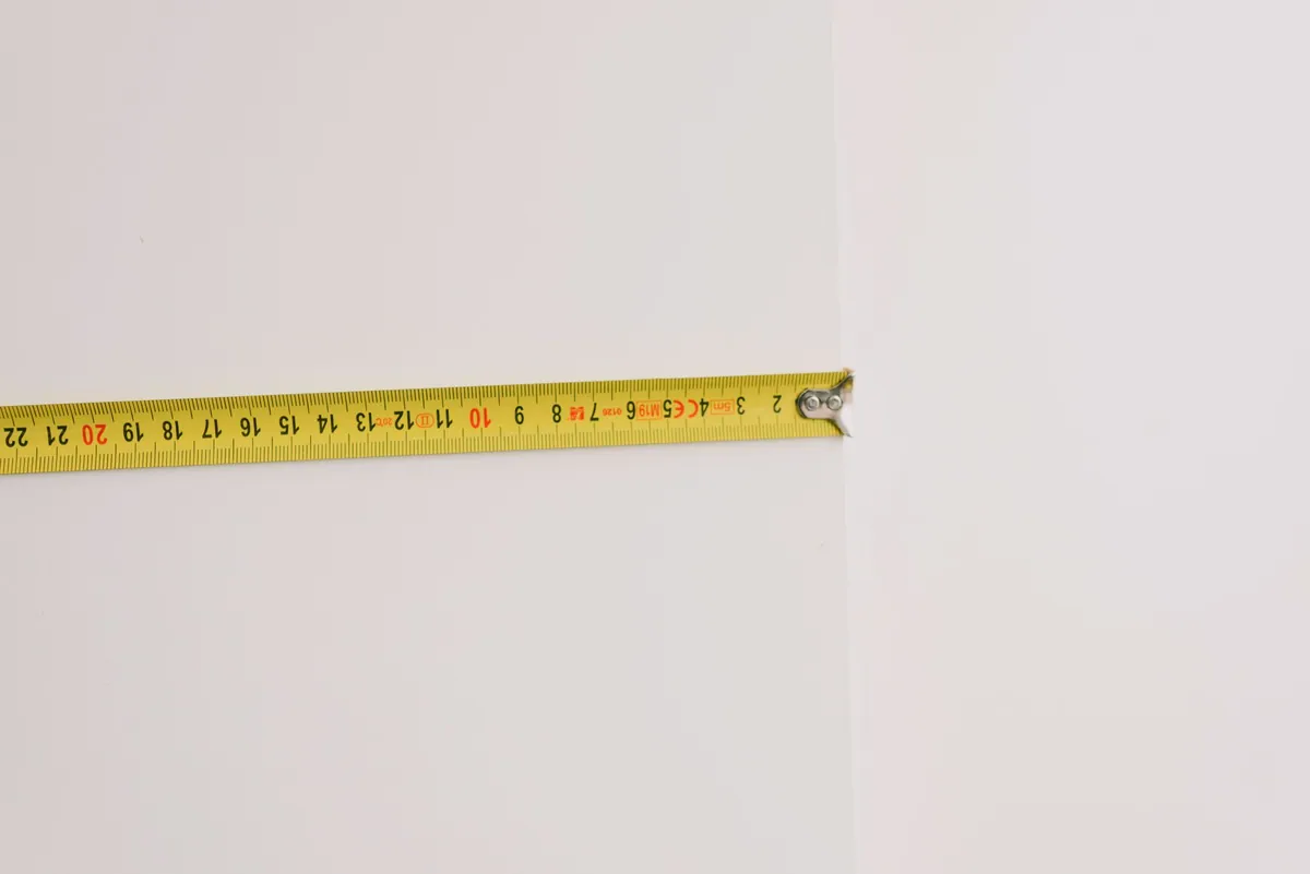 Measuring tape laid across a wooden floor beside an area rug, showing how to measure rug size